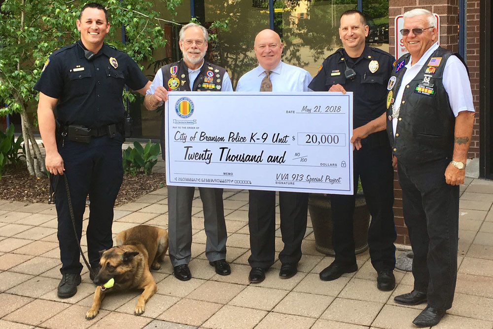 Giving Big
Branson Police Officer Frank Hirahara and Assistant Police Chief Eric Schmitt, both in uniform, receive a $20,000 check from Post 913 of the Vietnam Veterans Association. The Branson Police Department will use the donation – the largest in Post 913 history – to purchase and train a new police K-9.